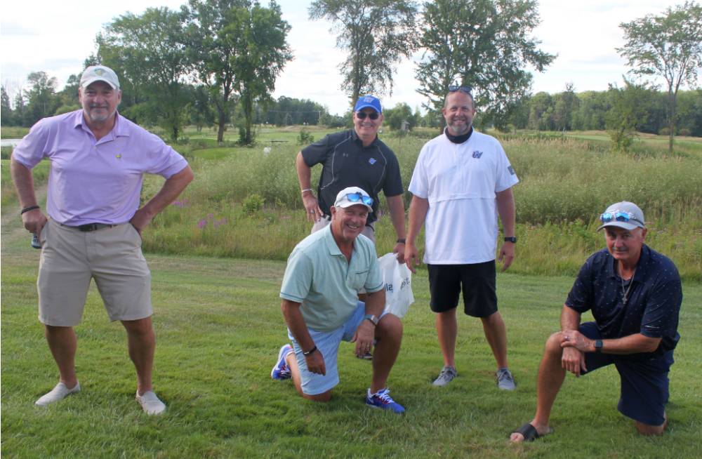 five alumni taking a picture on the golf course